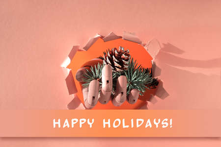Merry Christmas, hand with fir twigs and cone through paper hole. Creative minimal concept background with long shadow on beige, orange paper.の写真素材