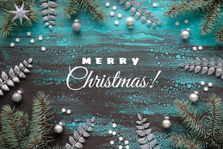 Merry Christmas text. Xmas border with fir twigs, glass baubles and exotic fern leaves and light garland. Acrylic background in turquoise, brown. Flat lay, top view.の写真素材