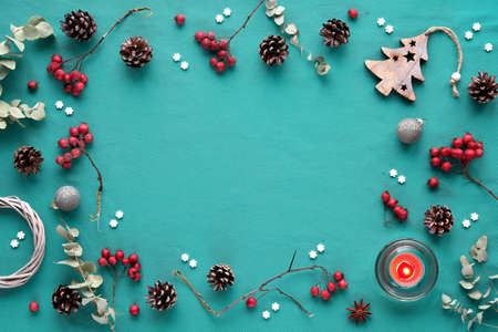 Natural low impact Xmas decor. Christmas background in turqiouse and red, copy-space. Flat lay, hawthorn berry, eucalyptus, wattle wreath, Xmas tree toy, balls, candle, pine cones, white snowflakes.の写真素材