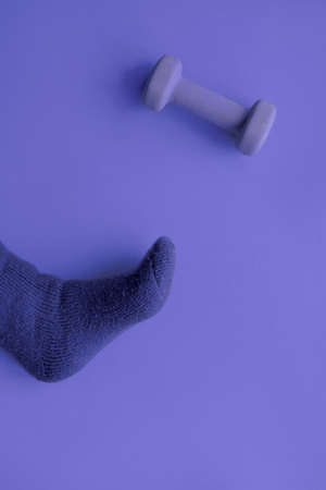 Purple very peri monochrome abstract paper background with foot in warm sock and dumbbell. Simple minimal sport background.の写真素材