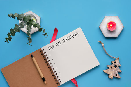 New Year resolutions. Text in spiral notepad, notebook. Tea light candle. Top view, flat lay, mint green table. Eucalyptus twigs, ribbon as bookmark. Xmas tree, wintertime Christmas decor.の写真素材