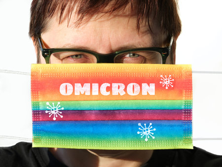 Omicron covid variant of concern. New coronavirus strain. Rainbow face mask in female hands....