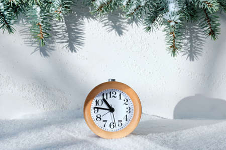 Winter time. Wood alarm clock, sunsne, snow and fir twigs. Sunlight, strong shadows. Wintertime creative minimal concept.の写真素材
