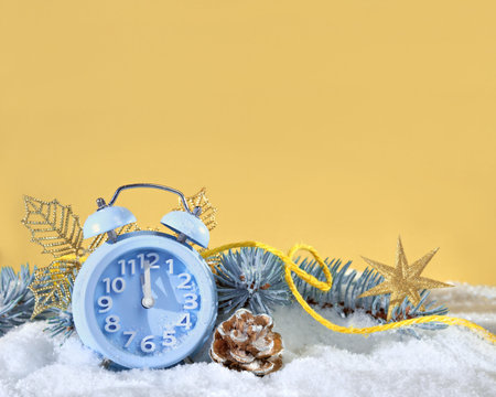 Christmas decor, mint blue alarm clock on golden yellow background. Sunshine, snow and fir twigs. Sunlight with shadows. Xmas creative greeting card design, copy-space.の写真素材