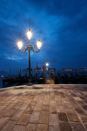 Italy, Venice Embankment at night. Historical lamp post with goldolas and San Giorgio di Maggiore. Monochromatic travel background image.の写真素材