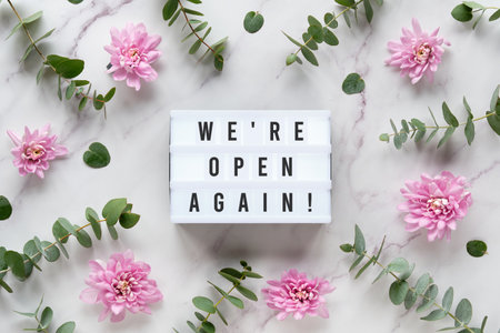 Come in we are open. Lightbox with text. Wintertime eucalyptus and pink chrysanthemum flowers. Winter flat lay. Top view on off white marble.の写真素材