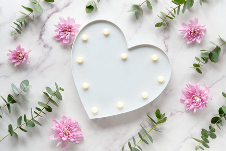 Heart shape lightbox. Wintertime eucalyptus and pink chrysanthemum flowers. Winter flat lay. Top view on off white marble table.の写真素材