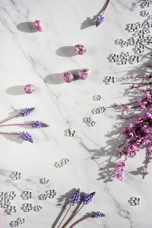 Pink colored quail eggs. Small pink flowers and grape hyacinth on off white marble. Easter off white...