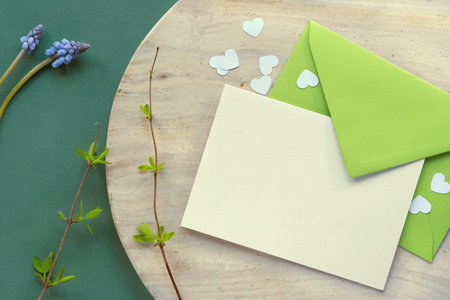 Spring background in shades of green. Paper envelope with blank greeting card and heart confetti on...