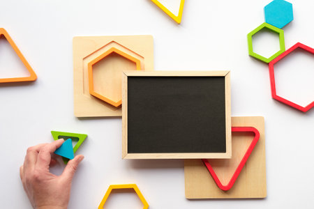 Geometric wood figures and blackboard blackboard. Nested wood triangles and hexagons in rainbow colors. Turquoise triangle in human hand.の写真素材