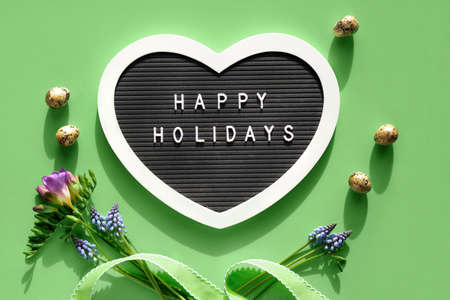 Happy Holidays text on felt heart shaped letter board, letterboard. Spring flat lay on light green. Pink flowers.の写真素材