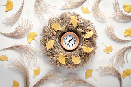 Autumn time background. Wood alarm clock in dry grass wreath. Of white flat lay background with ginko leaves and pampas grass.の写真素材