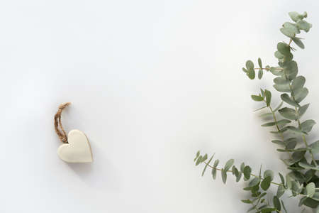 Fresh eucalyptus leaves and twigs. Wooden heart trinket with white enamel and hemp cord. Top view on off white tabletop. Simple, minimal flat layの写真素材