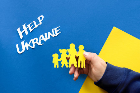 Help Ukraine text on blue background. Helping hands, male and female, holding Ukrainian family, yellow paper silhouette. Flat lay, top viewの写真素材