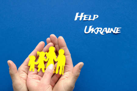 Help Ukraine text on blue background. Helping hands, male and female, holding Ukrainian family, yellow paper silhouette. Flat lay, top viewの写真素材