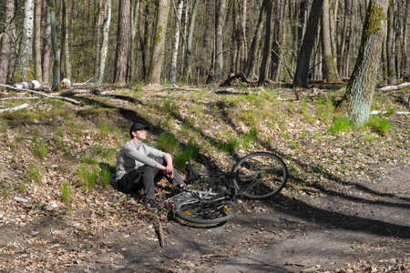 Female biker resting next to her bicycle in Spring forest. Country road, bike way, foot path through Spring greenery.の写真素材