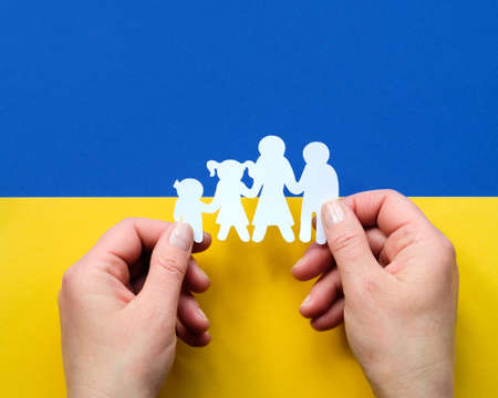 Hands holding paper silhouette of Ukrainian family on blue yellow Ukraine flag background. Flat lay, top view on paper background.の写真素材