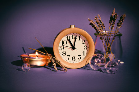 Still life on purple background with wood alarm clock. Dry lavender, tea light with flame. Glass...