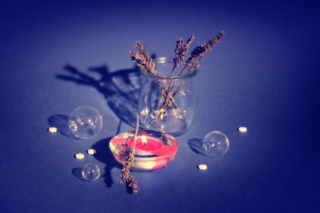 Still life on purple background. Dry lavender, tea light with flame. Glass spheres, bubbles.