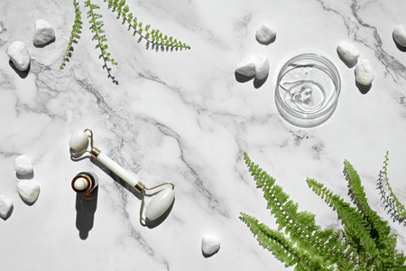 Self made moisturizer and green jade face roller. Exotic fern leaves on off white marble background.