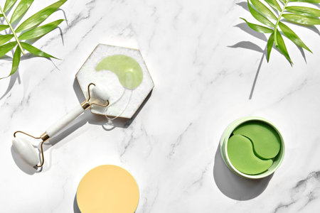 Hydrogel pads and chinese stone roller on off white marble stone background with palm leaf shadow