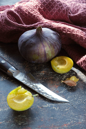 Closeup on Autumn fruits, purple fig, yellow pear and yellow plums with kitchen knife. Dark textured...