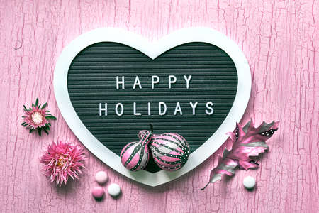 Heart shaped letter board with pink Fall decor. Text Happy Holidays on letterboard. Stripy pumpkins, dry leaves, flowers.の写真素材