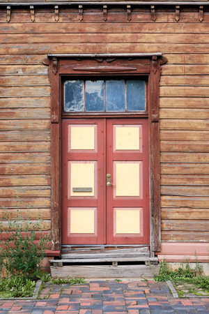 Old red wooden doors, entrance to wooden house with withered peeling brown paint on the walls in Tartu, Estonia.の写真素材