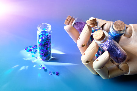Glitter powder, glittering product bottles in ooden dummy hand, artificial artistic wood model hand. Spilled glitter particles on table. Makeup, craft or other hobby supplies in neon shades.の写真素材