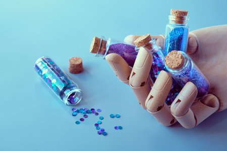Glitter powder, glittering product bottles in ooden dummy hand, artificial artistic wood model hand. Spilled glitter particles on table. Makeup, craft or other hobby supplies in neon shades.の写真素材