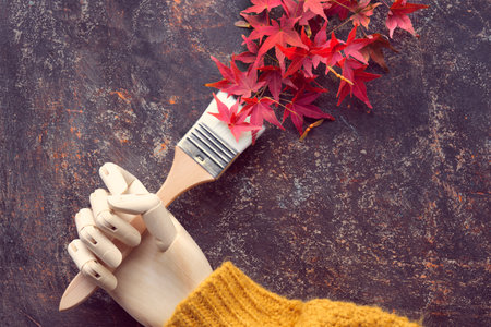 Paint brush, paintbrush with red oak leaves as paint. Brush in artistic model wooden hand in orange sweater. Autumntime colors, creative flat lay background.の写真素材