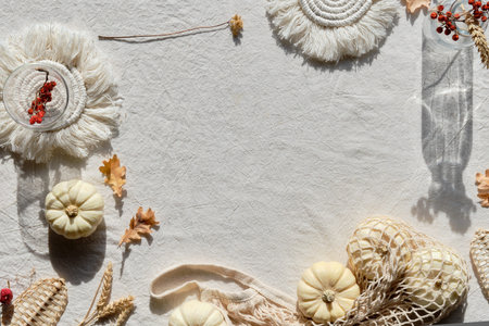 Off white textile background with natural Fall decorations. Flat lay, top view. Pumpkins in net bag,...