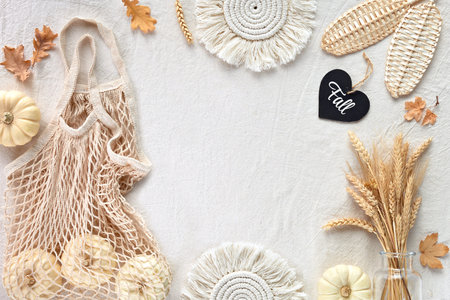 Off white textile background with natural Fall decorations. Flat lay, top view. Pumpkins in net bag,...