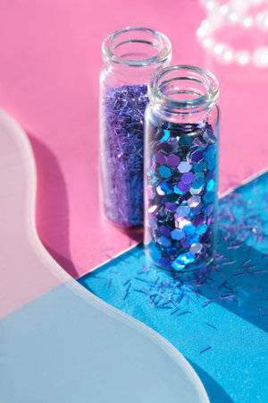 neon colored glitter products on pink sparkling background. Close-up on vials, bottles with various...