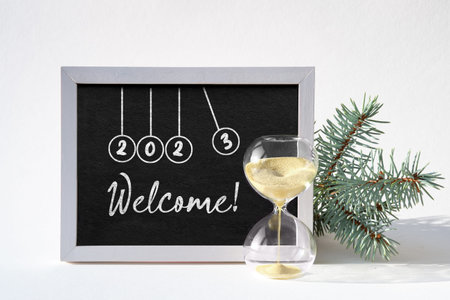 New Year 2023 in balls of newton cradle on blackboard. Caption, text Welcome 2023 on chalk board....
