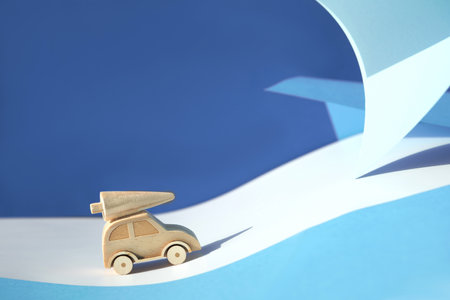 Wooden toy, silhouette of Christmas tree on toy car on colored layered paper background. Xmas holiday blue celebration background. Copy-space, place for text. Simple, minimal design.の写真素材