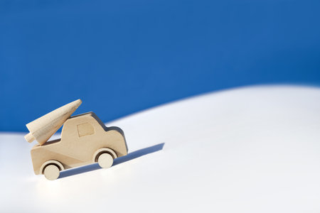 Wooden toy, silhouette of Christmas tree on toy car on colored layered paper background. Xmas holiday blue celebration background. Copy-space, place for text. Simple, minimal design.の写真素材