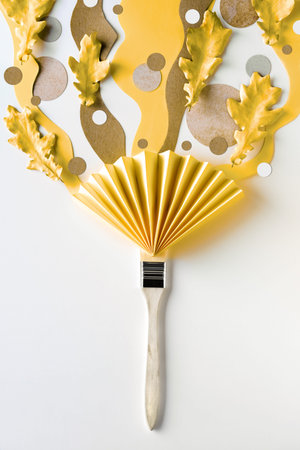 Brush loaded with paint made from Autumn yellow oak leaves and organic paper shapes in yellow,...