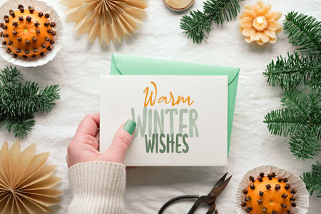 Fragrant pomander balls handmade from tangerines with cloves. Handmade paper stars from brown paper. Flat lay on off white textile with fir twigs. Caption Warm winter wishes on paper card in hand.の写真素材