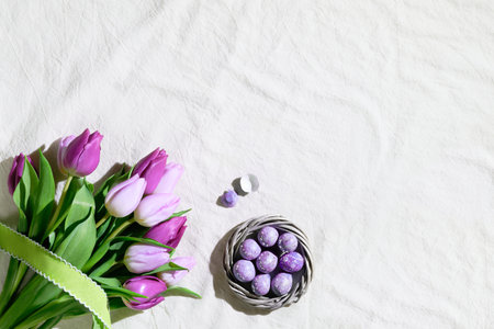 Easter corner composition with bunch of pink magenta tulips and nest, wreath with quail Easter eggs. Flat lay on off white textile tablecloth. Greeting card, webpage design, copy-spaceの写真素材