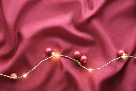 Viva Magenta color of the year 2023. Dark red Christmas background. Flat lay with Xmas baubles and garland of electric festive lights on red silk textile background.の写真素材
