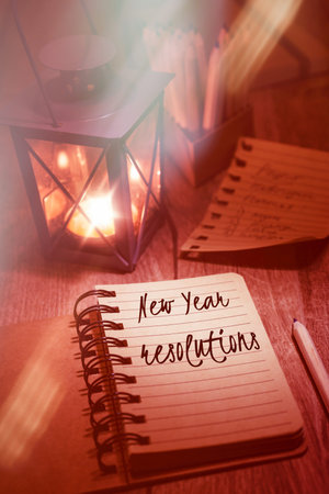 New Year resolutions handwring in notebook. Tea light in n metal vintage lantern, torn-out page and...
