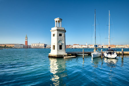 Marina and lighthouse tower on San Giorgio di Maggiore with city of Venice behind. Venezia, Italy, Europe. Sailing boats, yachts moored by pier.の写真素材