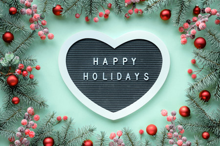 Christmas heart shaped text board, message greeting words Merry Christmas. Frame with fir twigs, berries, red baubles. Top view, flat lay, festive Xmas background on mint green paper background.の写真素材