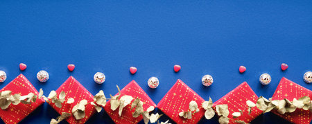 Wintertime red decorative border with gift boxes, disco balls and eucalyptus. Flat lay on blue linen...