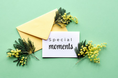 Text Special moments on paper card with mimosa flowers in yellow envelope on mint green background....