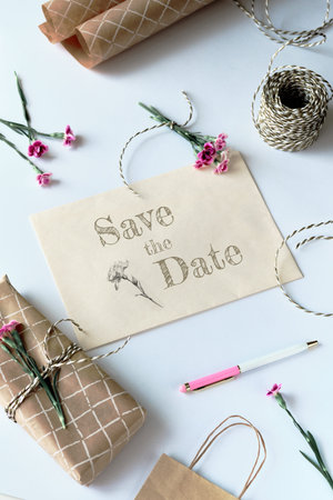 Envelope and greeting card with fresh carnation flowers. Text Save the date on the card.