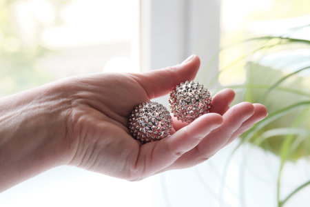 Silver metal magnetic balls in female hand. Spiky tool for hand massage. Close-up on middle-aged handの写真素材