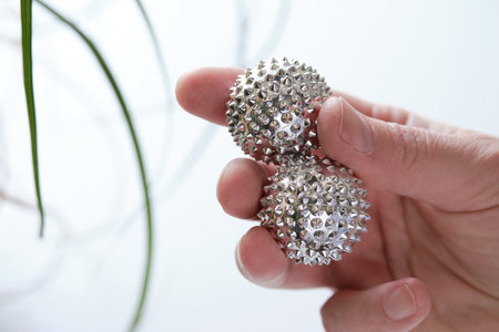 Silver metal magnetic balls in female hand. Spiky tool for hand massage. Close-up on middle-aged hand.の写真素材