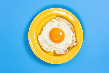 A fried egg on a yellow plate on a blue backgroundの素材